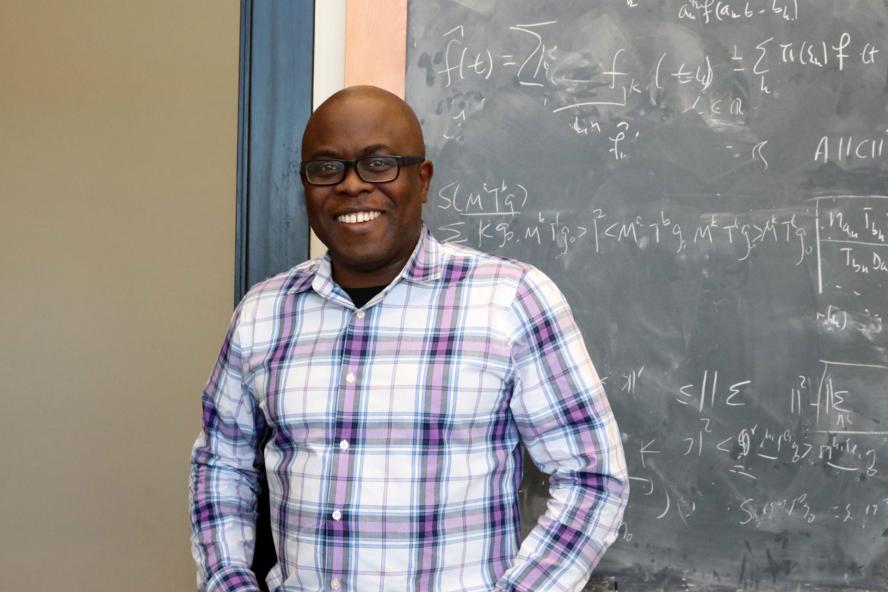 Kasso Okoudjou standing in front of a blackboard