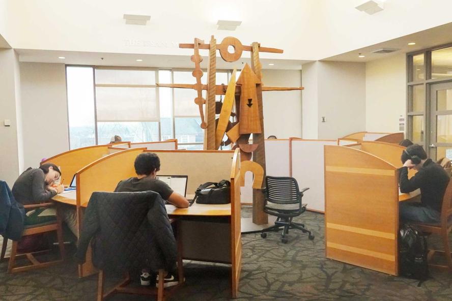 Students working at cubicle desks set in a circle near a large sculpture in Tisch Library