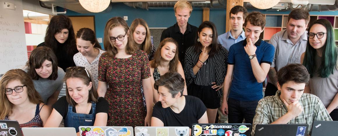 Students working in a classroom looking at computers with Professor Moon Duchin